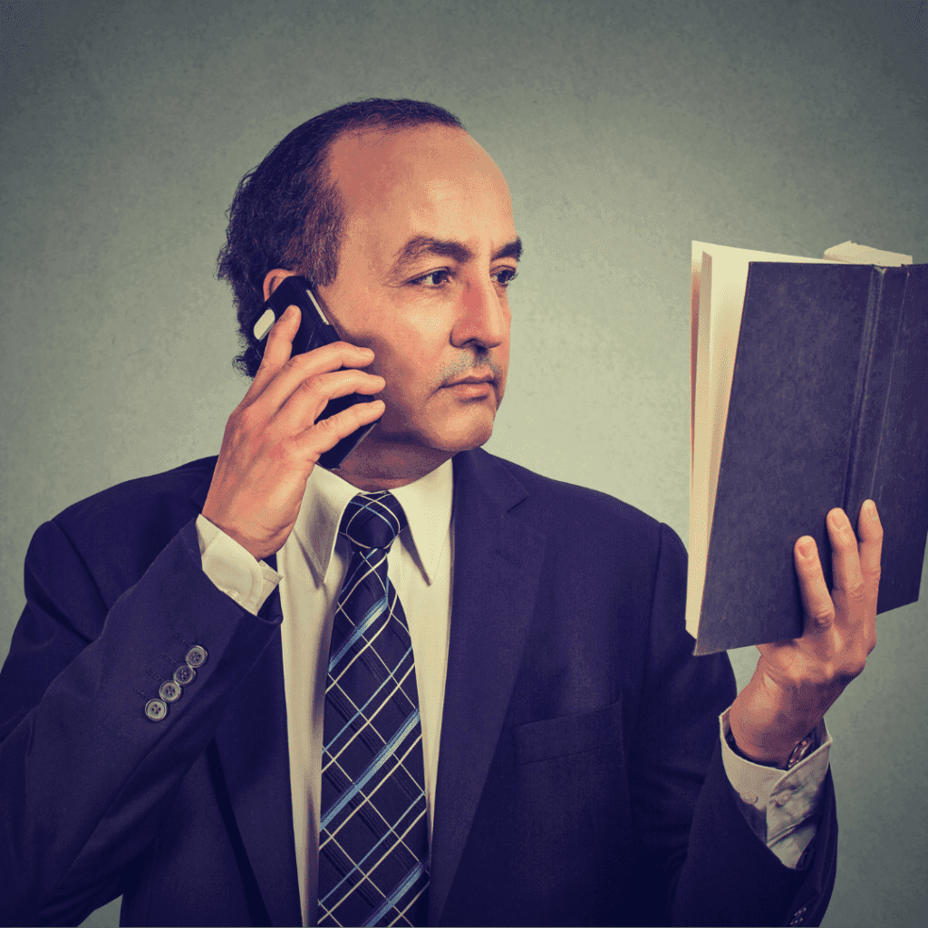 a man holding a phone while looking at a book